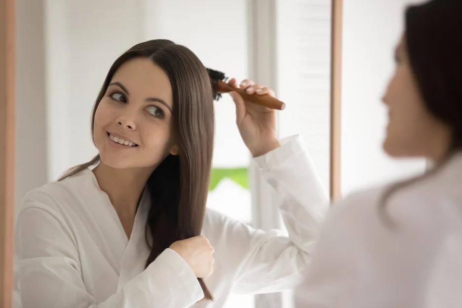 a woman checks her hair in front of the mirror after pdrn treatment for hair regrowth