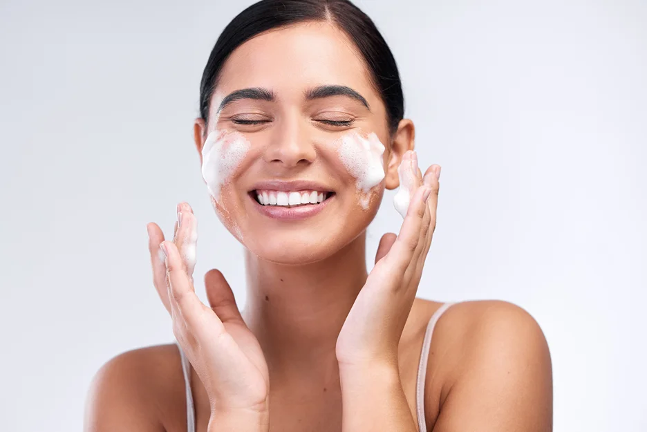 Smiling woman cleansing her face with a foaming facial cleanser