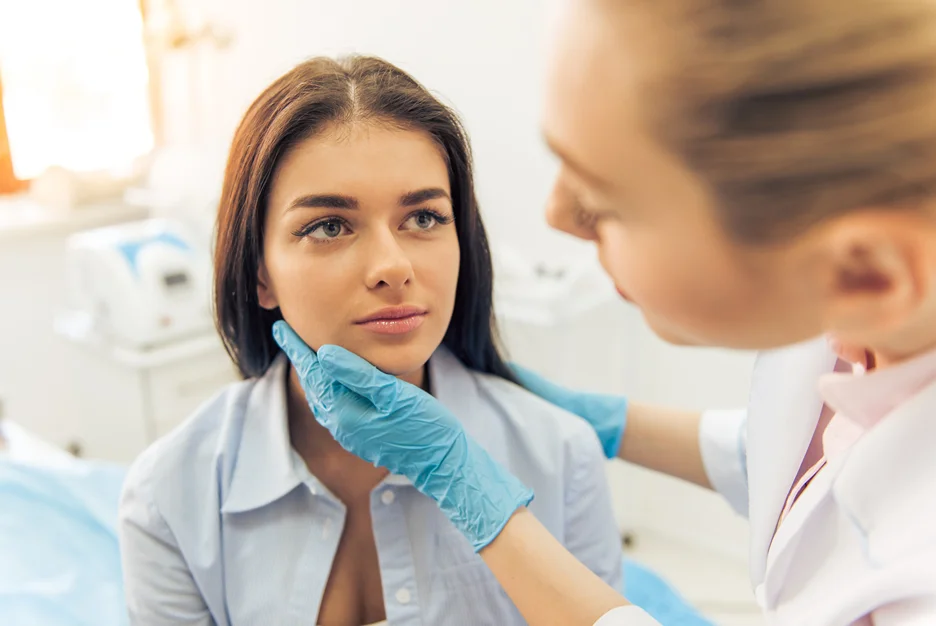 Practitioner in blue gloves assessing a client's chin and jawline