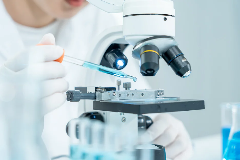 Researcher pipetting a blue sample onto a microscope slide in a laboratory