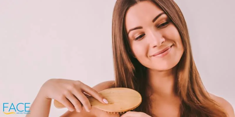 Portrait of young attractive woman combing her shiny healthy hair with wooden brush