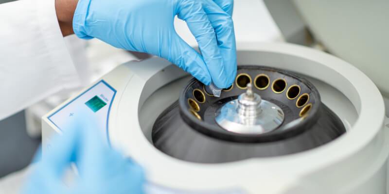 Selective focus shot of a medical researcher's hands as they load a centrifuge with samples