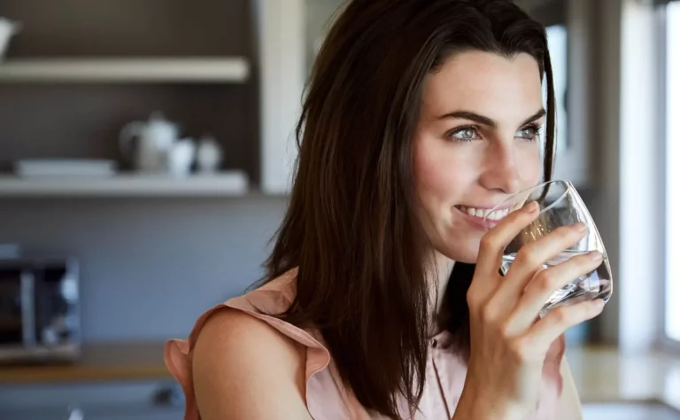 Beautiful woman drinking water and smiling in kitchen