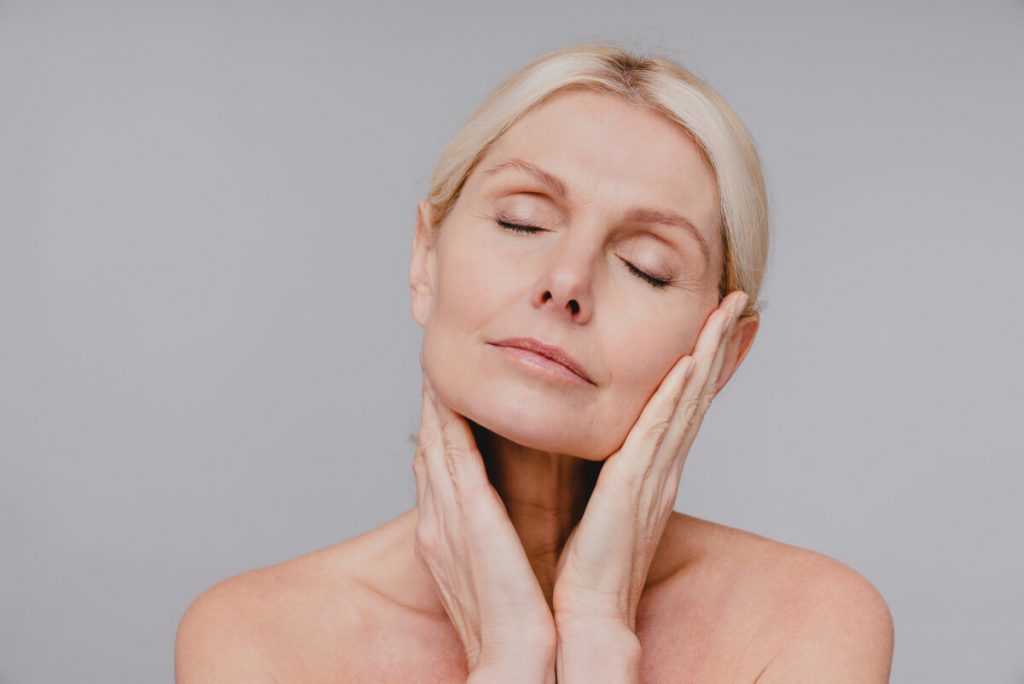 Beautiful aged white woman touching her clean pure face with her eyes closed