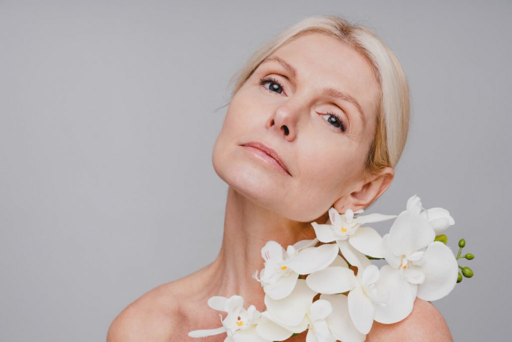 Beautiful mature woman with pure skin and orchid branch isolated over grey background