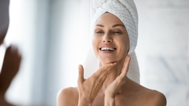 Happy confident young lady with towel on head look in bathroom mirror