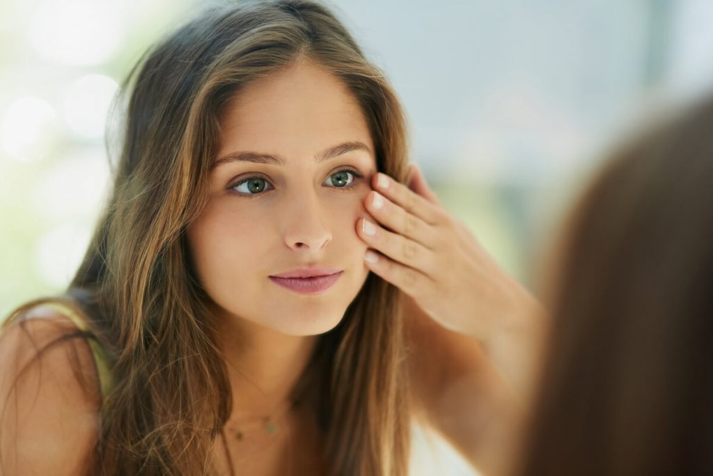 Shot of an attractive young woman touching her skin in front of the mirror