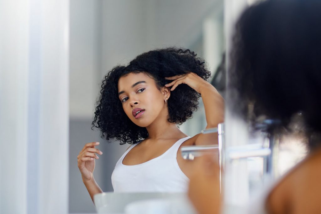 An image of a beautiful young woman looking in the mirror in her bathroom