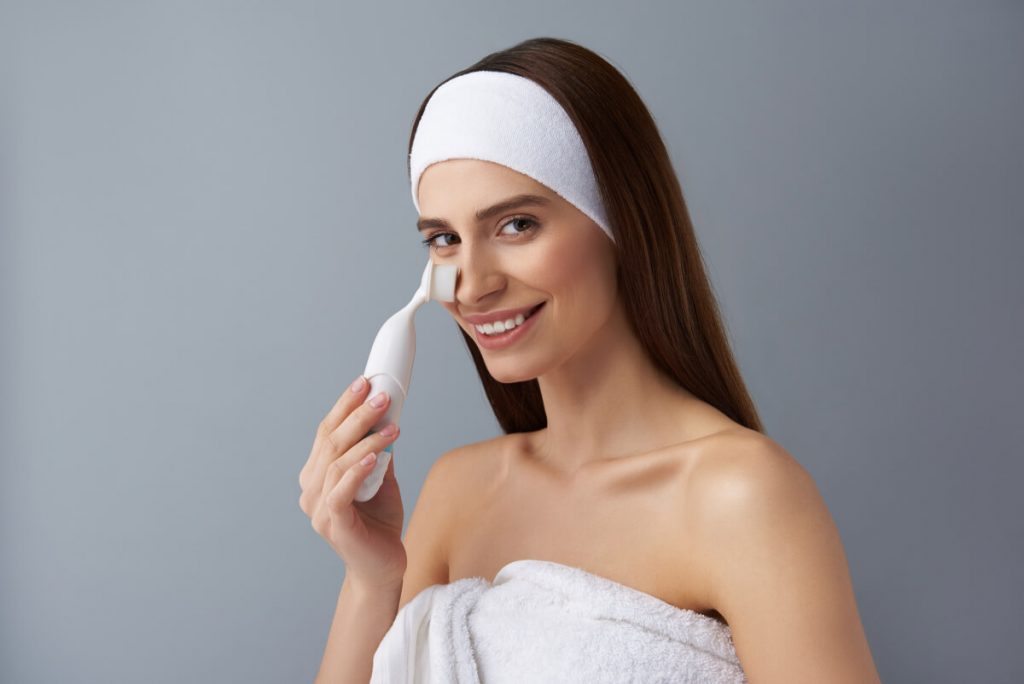 Charming young woman using pore cleansing brush