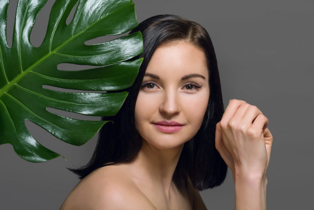 Studio beauty portrait of young brunette with natural make-up perfect skin with green exotic leaf 