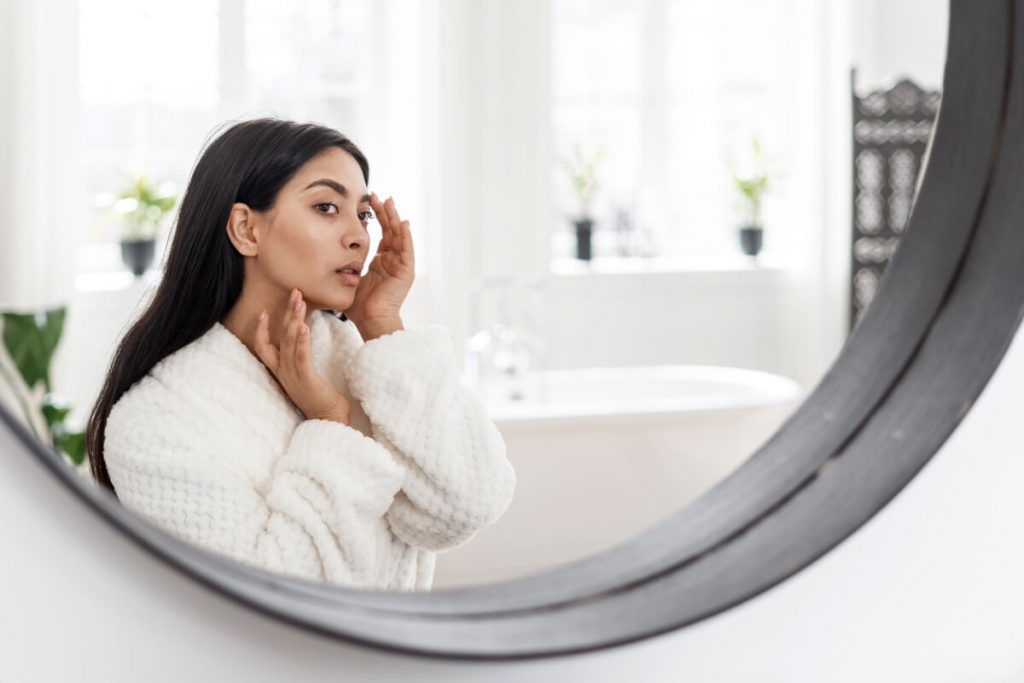 Young asian woman looking at mirror, checking skin