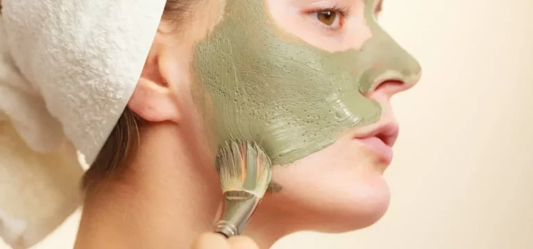 Woman applying with brush clay mud mask to her face