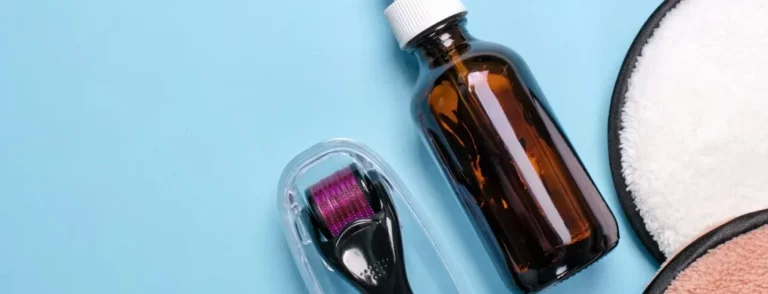 Derma roller and serum bottle on blue background