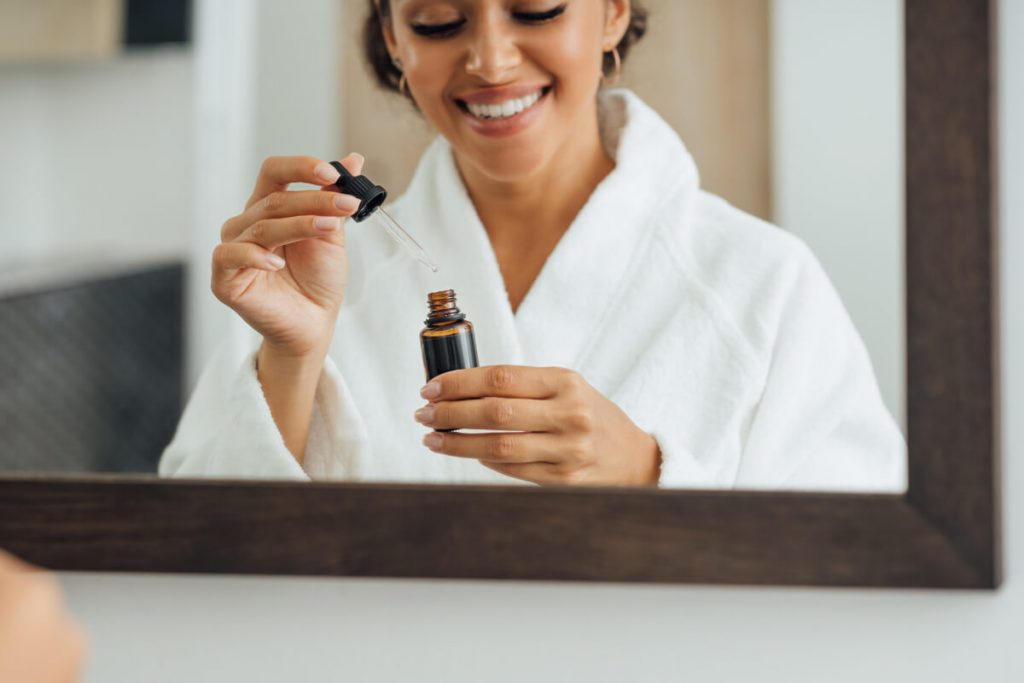 Close up of female hands holding a dropper and bottle with serum in bathrrom