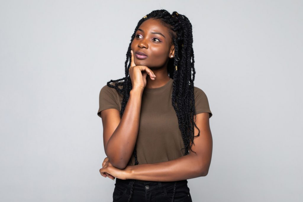 Portrait of a young african woman thinking with hand on chin on gray background