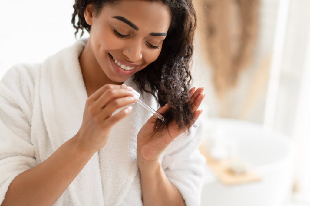 Woman Applying Serum On Damaged Dry Hair In Modern Bathroom At Home