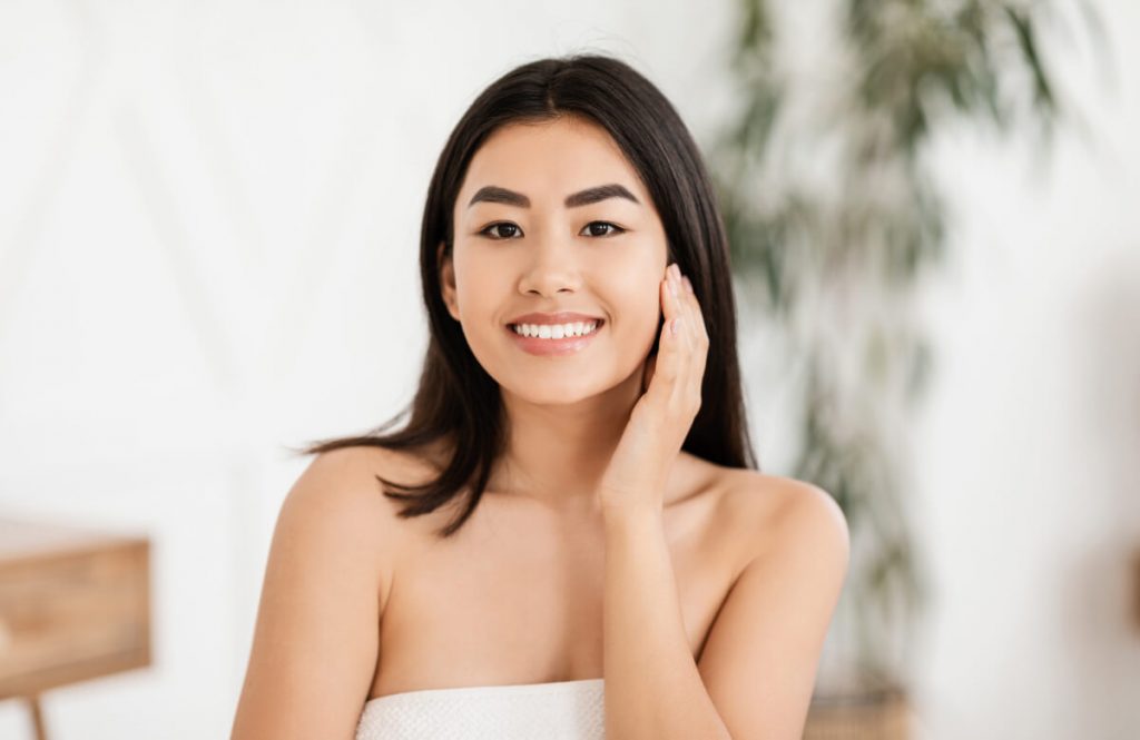 Happy asian woman wrapped in towel touching her face