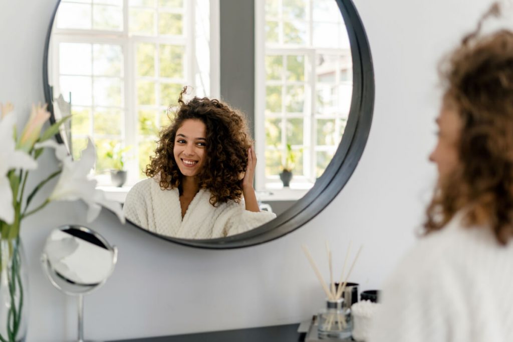 afro american woman in bathrobe looking on mirror at bathroom