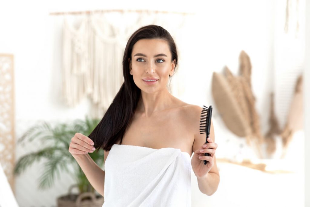 brunette female in towel with comb enjoys perfect long hair