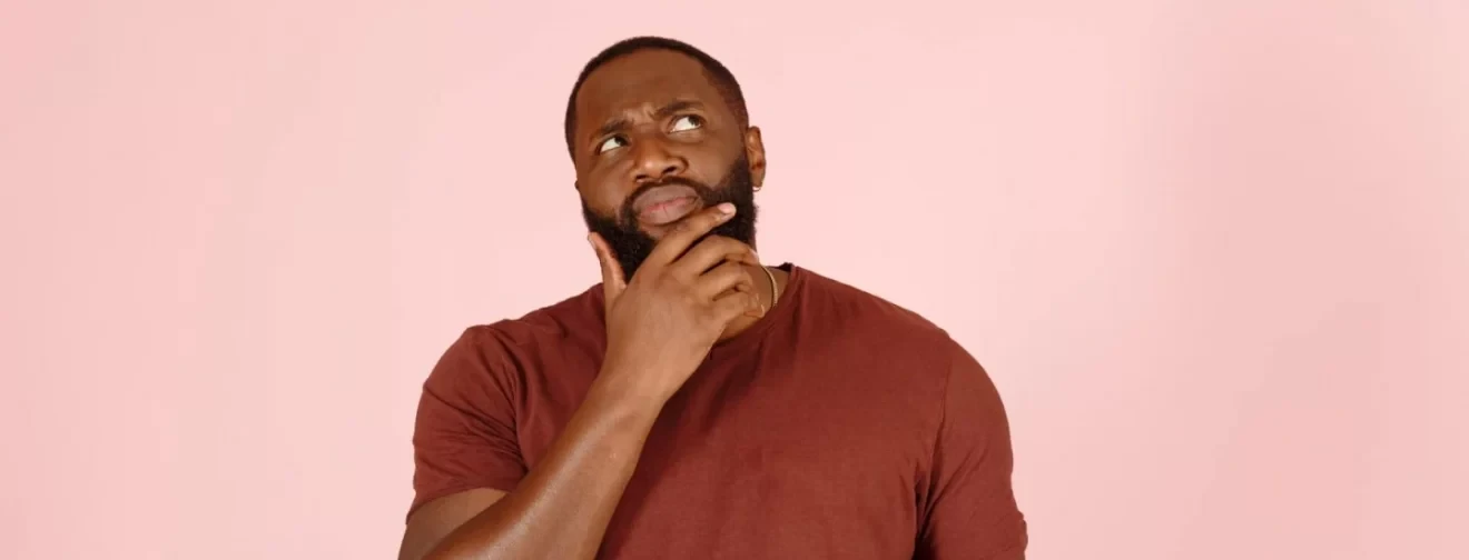 An afro American man touching his beard in pink background