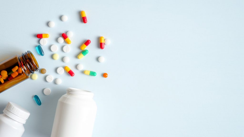medical bottles and medication pills spilling out on to pastel blue background