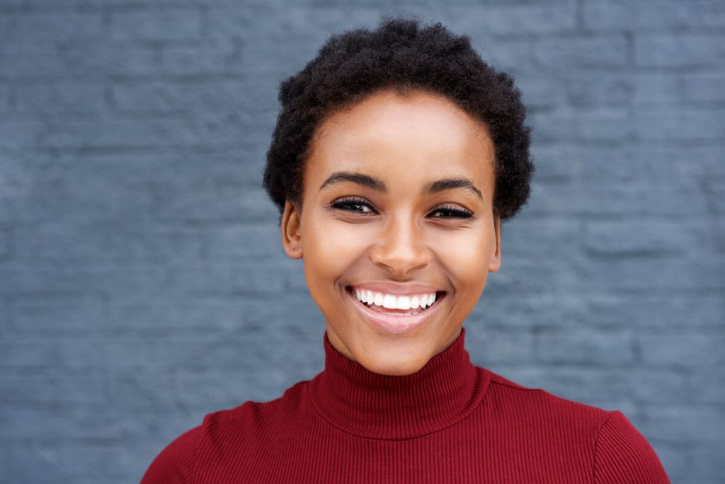 Close up portrait of young african woman smiling against gray wall