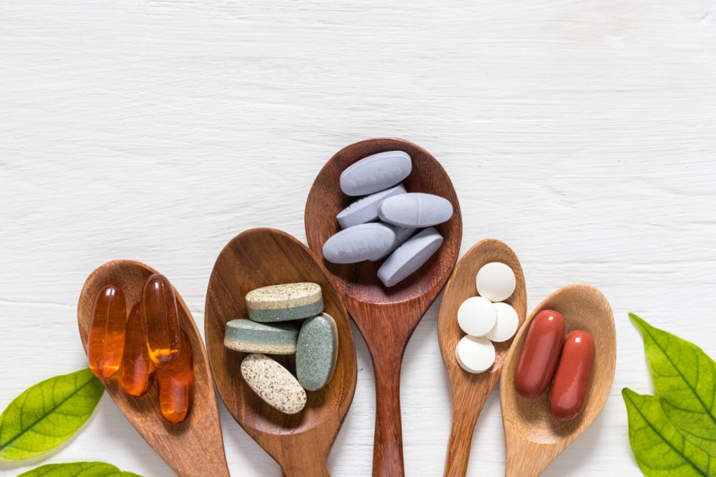 Variety of vitamin pills in wooden spoon on white background with green leaf