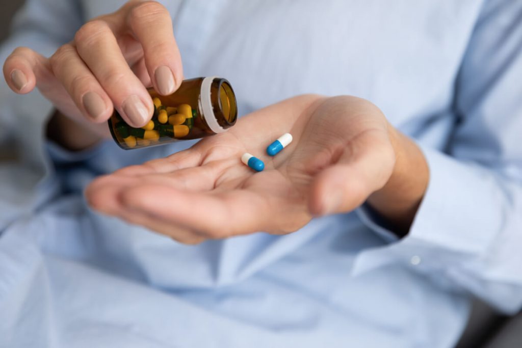 ill woman hold two pills on hand pouring capsules from medication bottle