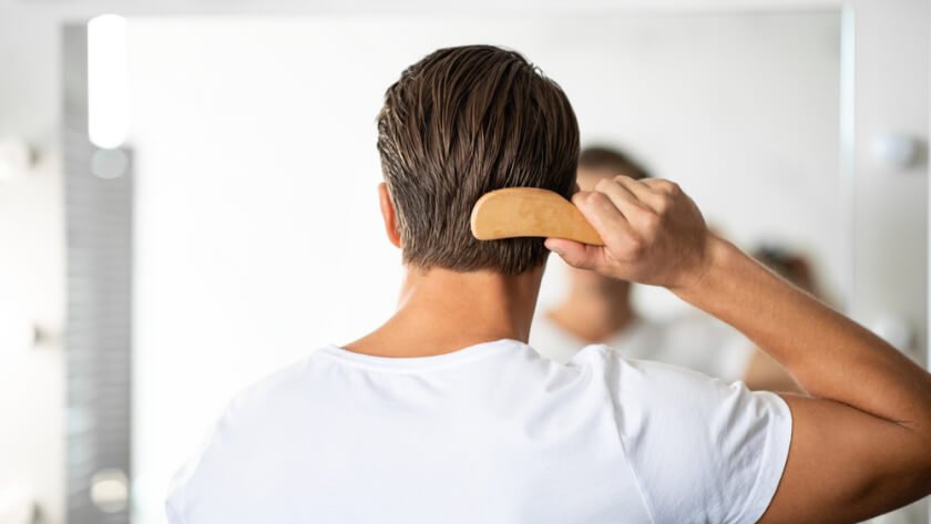 Close up rear view of young man hairbrushing with comb, looking in mirror