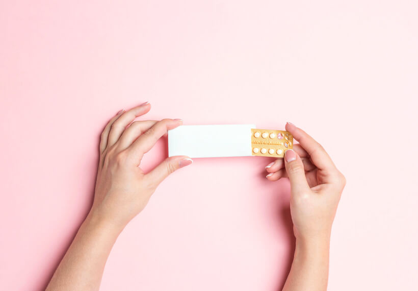 Female hands holding birth control pills on pink background