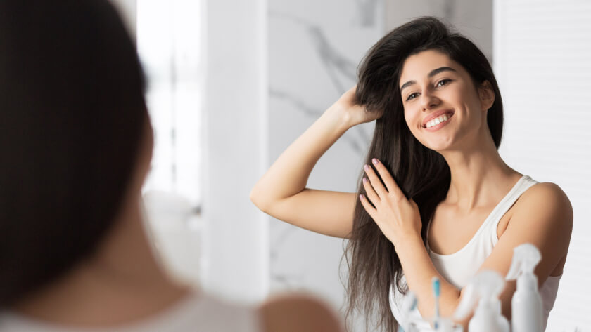 Smiling Girl Touching Hair Looking In Mirror In Bathroom