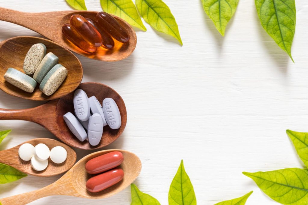 Variety of vitamin pills in wooden spoon on white background with green leaf