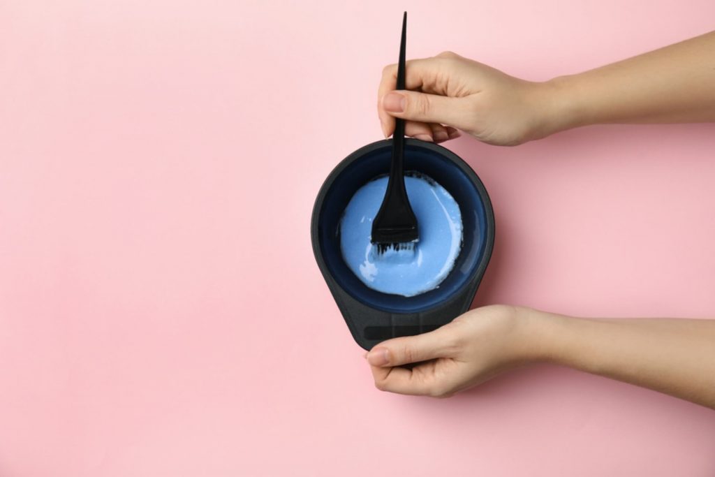 Woman preparing dye for hair coloring on pink background