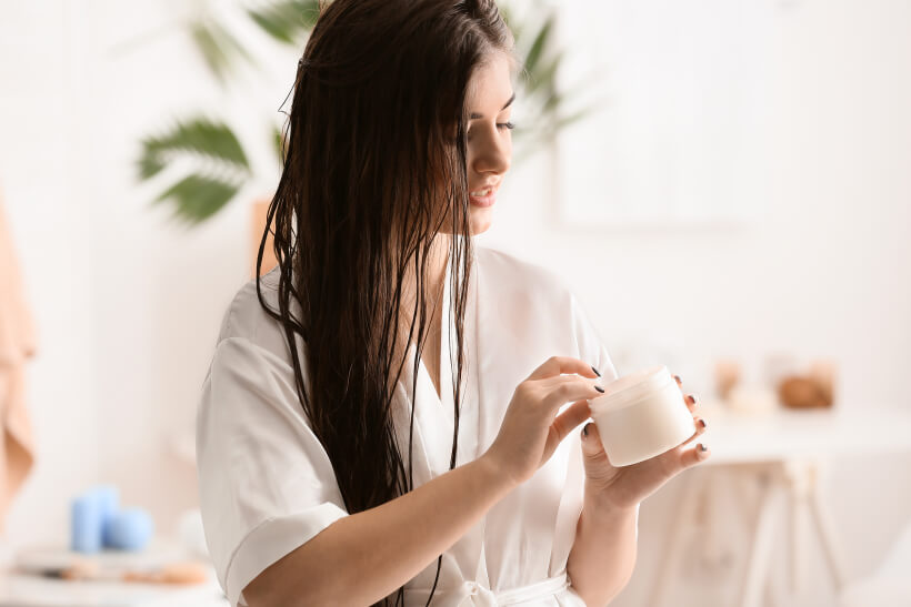 Young woman applying cream on beautiful long hair in bathroom