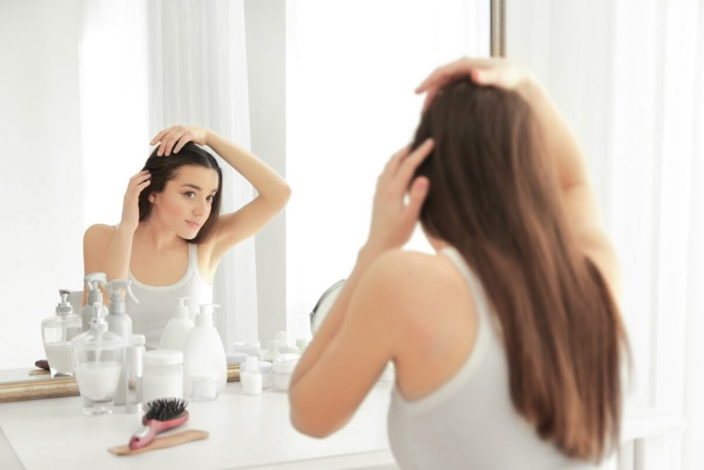 Young woman with hair loss problem in front of mirror at home