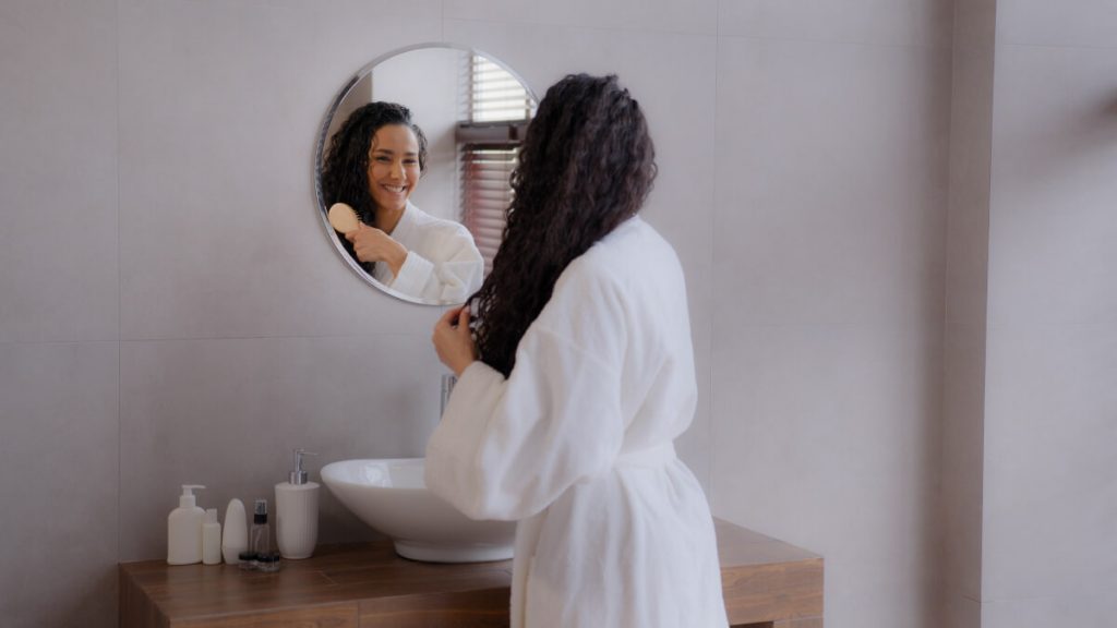 woman brushing her hair after prp treatment in the bathroom while looking at the mirror