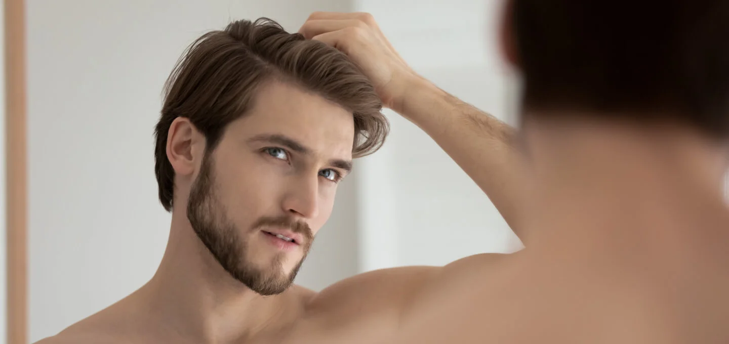 Young shirtless guy looks in mirror touching his hair