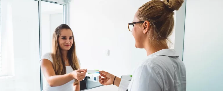 Young nurse or assistant at the receptionist desk greeting a female patient