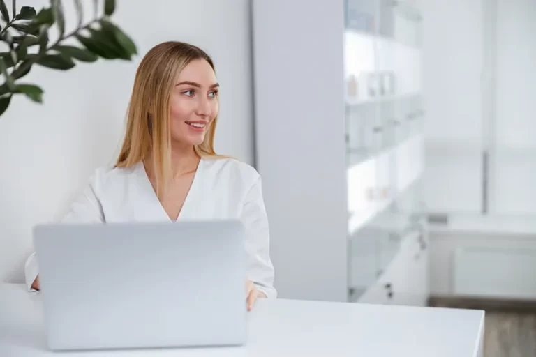 A smiling woman wearing a white uniform sitting in front of a laptop computer.