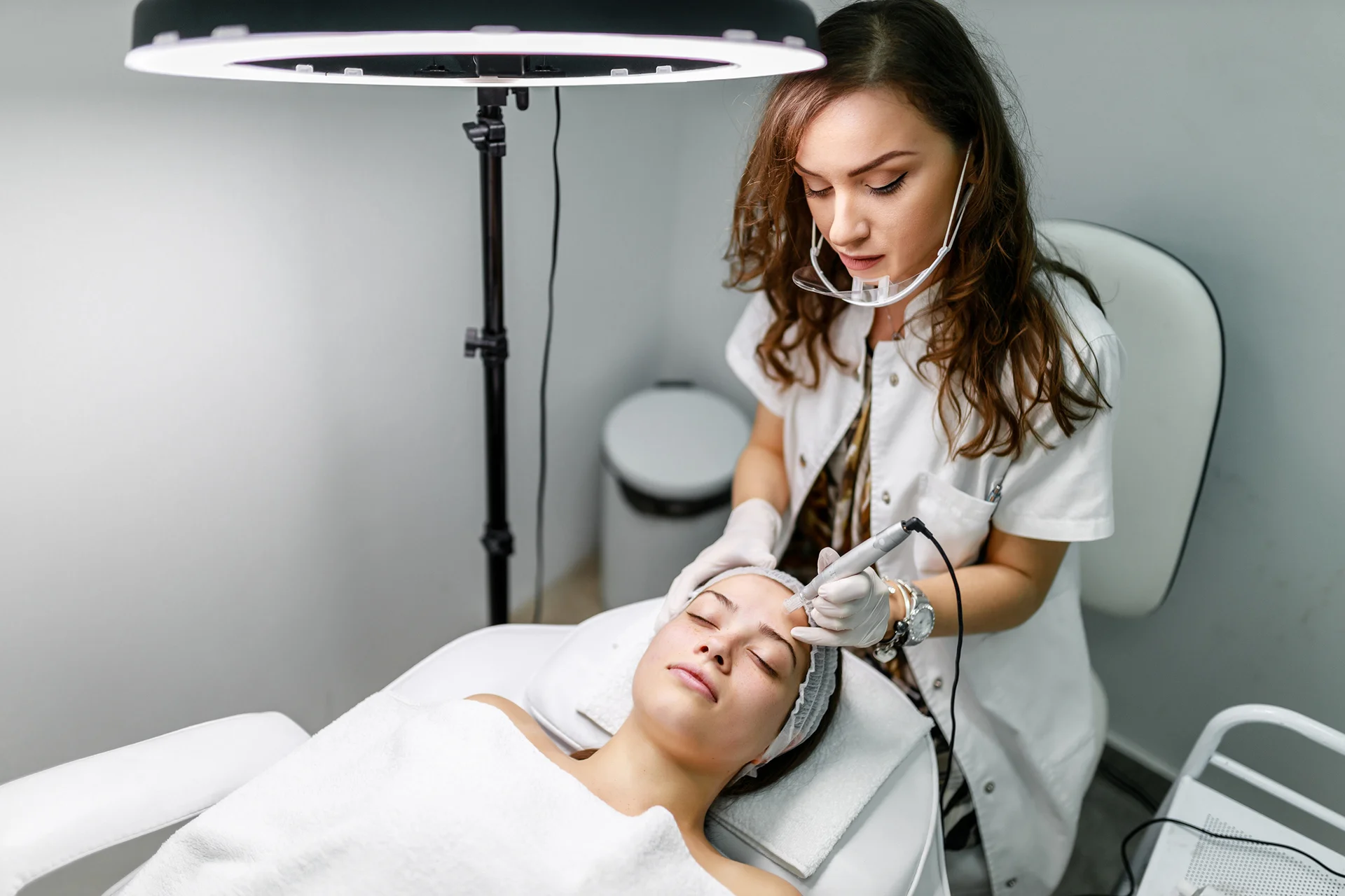 an aesthetician performs facial treatment procedure on her client.