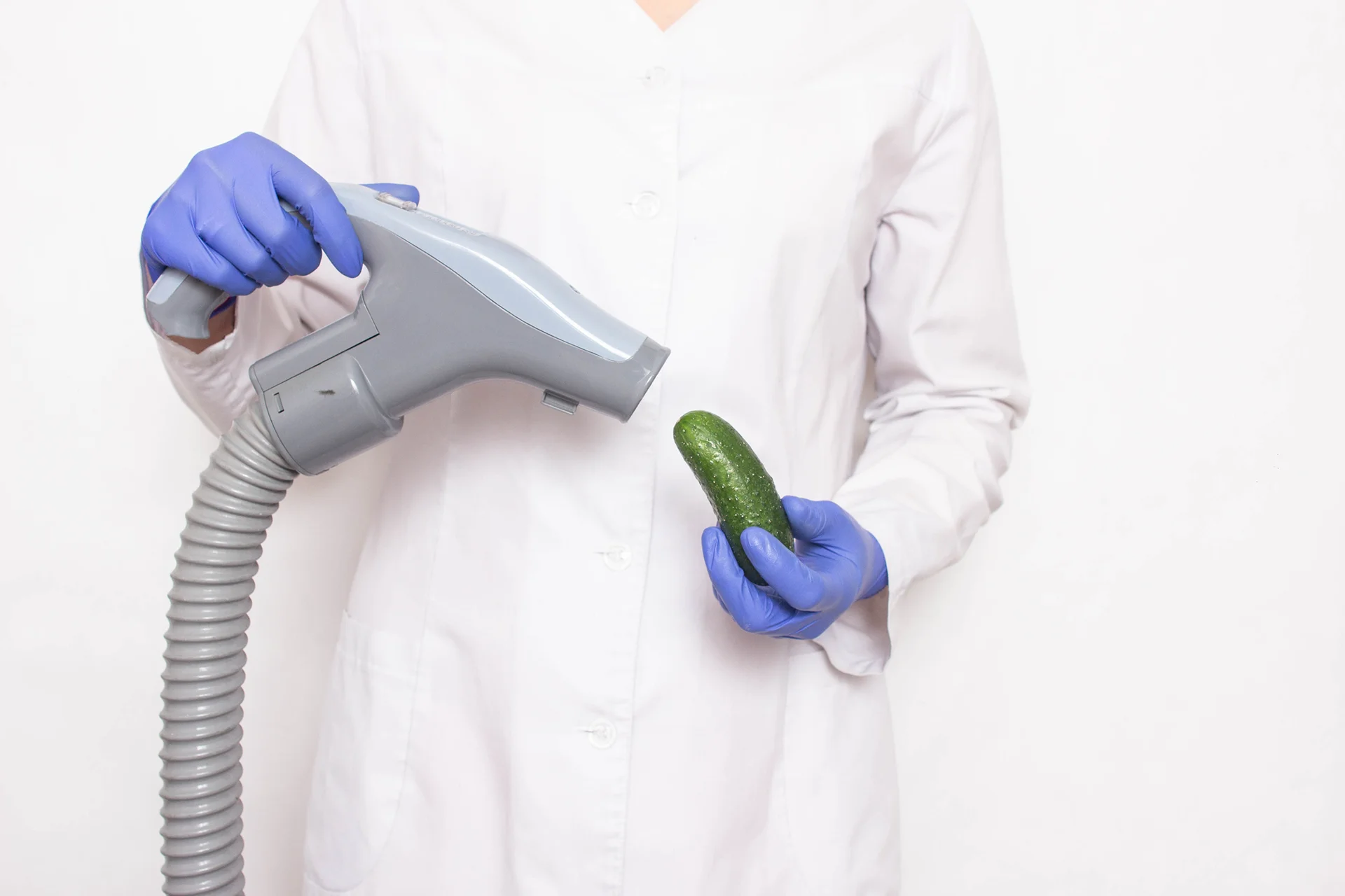Doctor holds a cucumber near the vacuum cleaner , the concept of increasing member in men with a vacuum pump