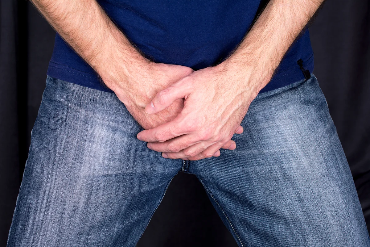 Man in shirt and jeans covering his groin area with his hands.