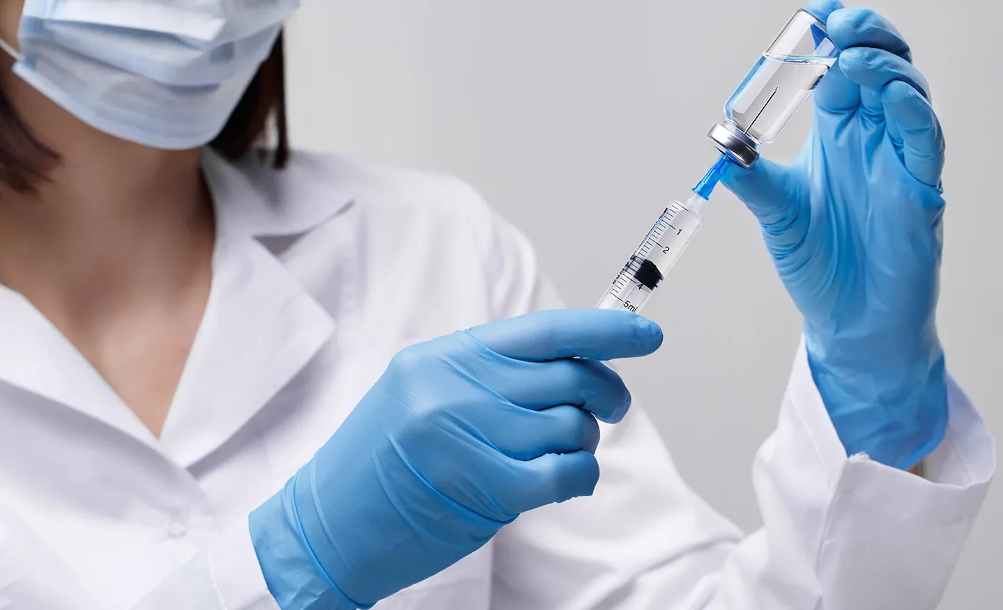 a medical professional holding a vial and a syringe with hypodermic needle