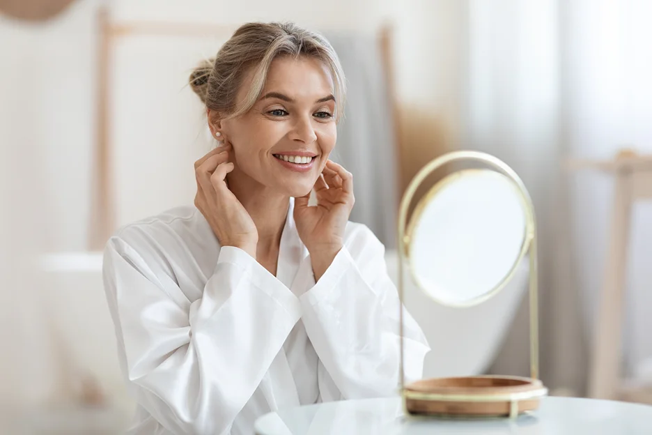 a woman checks her face in front of the mirror after using pdrn essence skincare