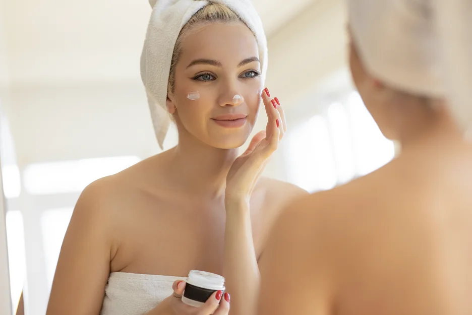 a woman checks her face in front of the mirror while applying pdrn skincare