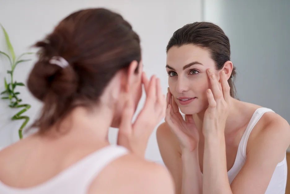 a woman checks her radiant skin in front of the mirror