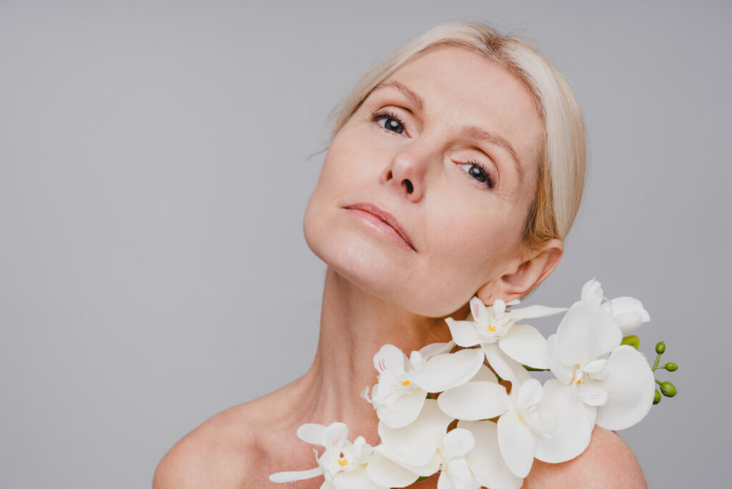 Beautiful mature woman with pure skin and orchid branch isolated over grey background