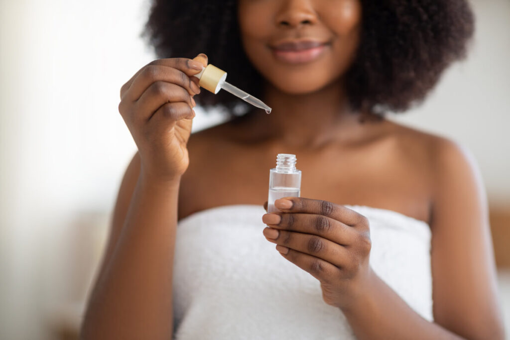 Cropped view of young black woman in bath towel applying face serum