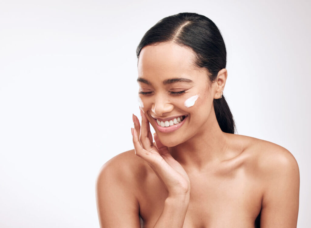 Studio shot of a beautiful young woman applying moisturiser to her face