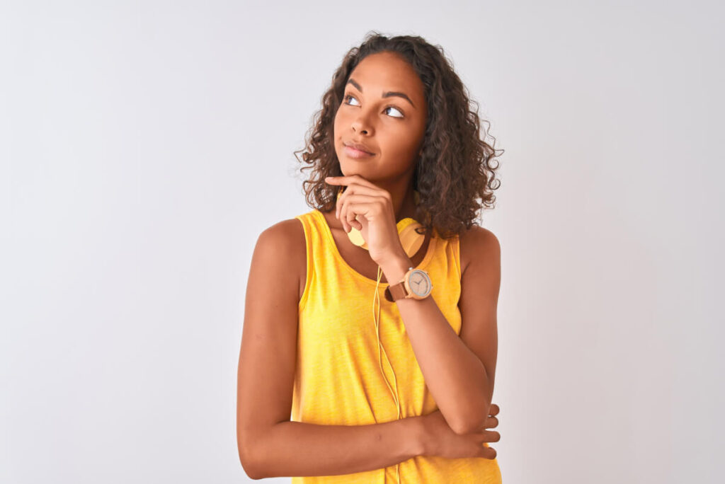 woman wearing yellow headphones over isolated white background with hand on chin thinking